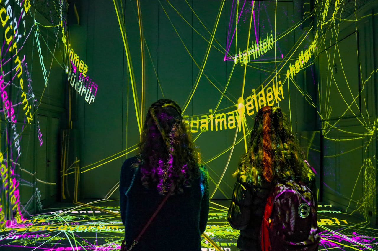 Two women observe a dynamic text projection art installation in a dark room.